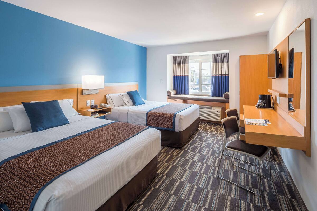 A hotel room with two beds, a desk, a chair, a TV, and a window with curtains.