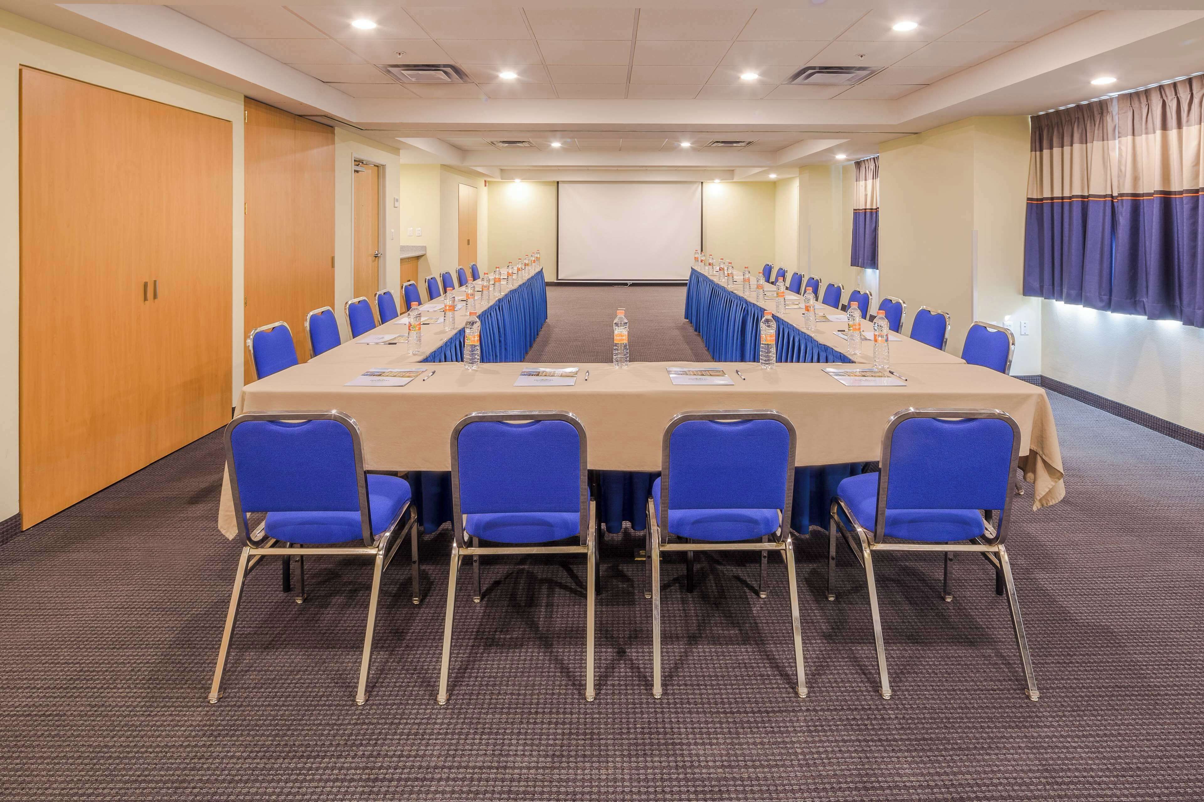 A conference room with a long table, blue chairs, and a projector screen.
