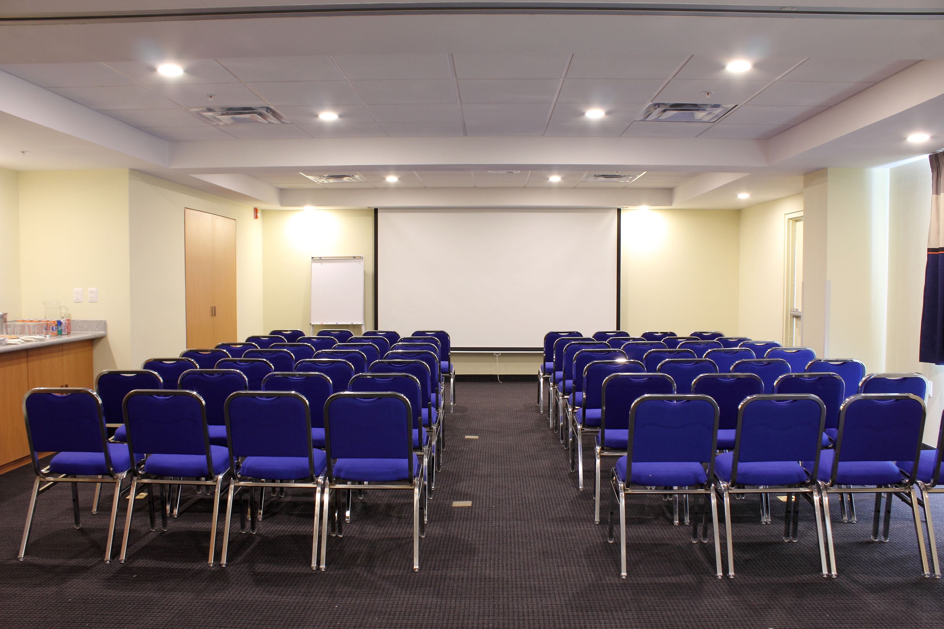 A conference room with rows of blue chairs, a projector screen, and a podium.