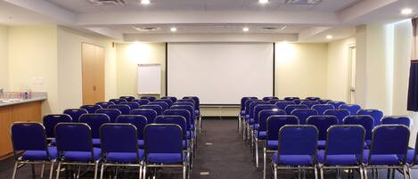 A conference room with rows of blue chairs, a projector screen, and a podium.