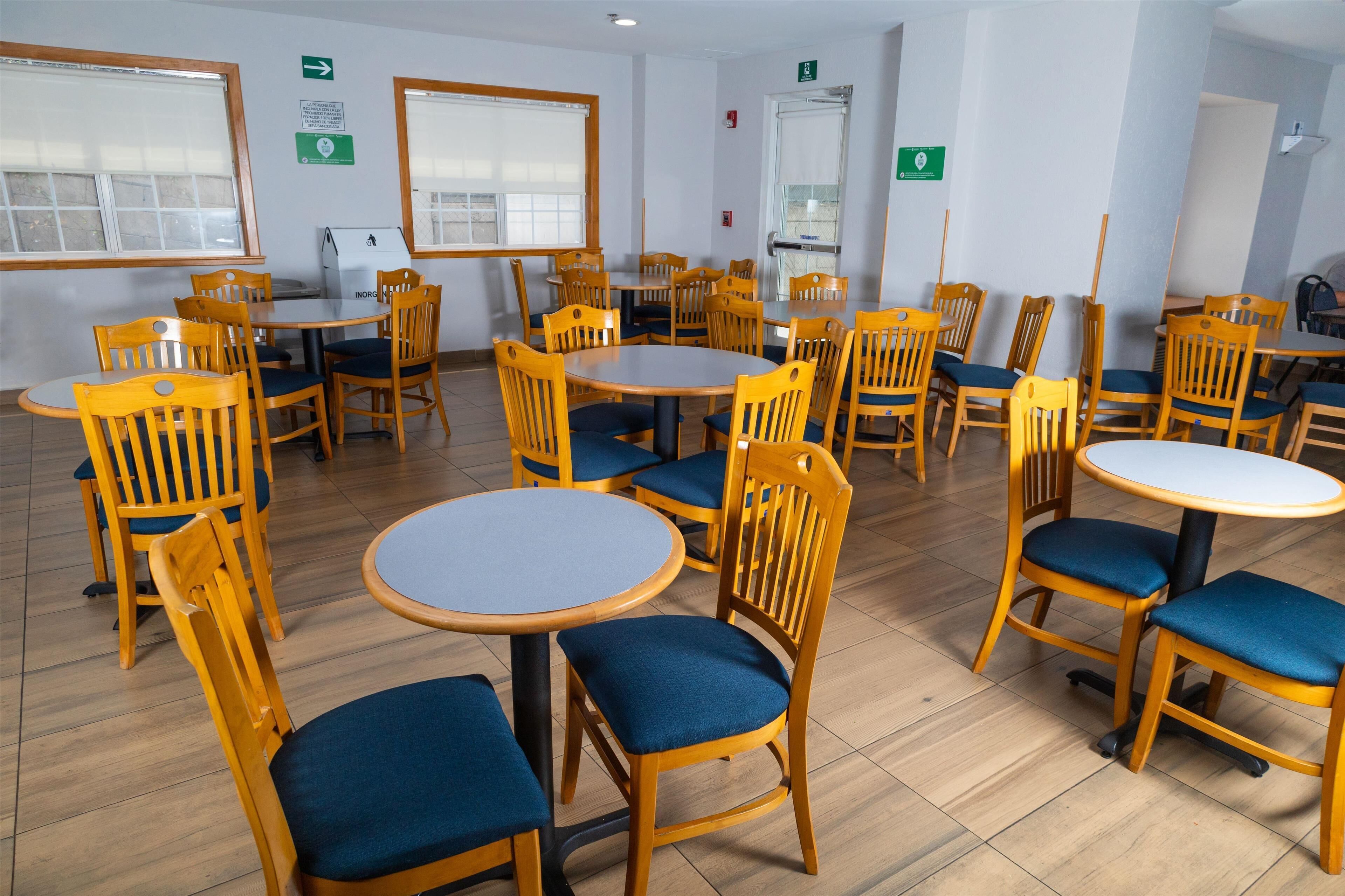 A dining area with multiple round tables and wooden chairs with blue cushions.