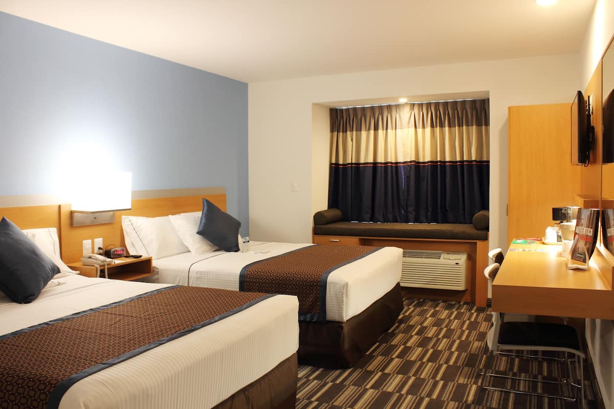 A hotel room with two beds, a desk, a chair, a TV, and a window with curtains.
