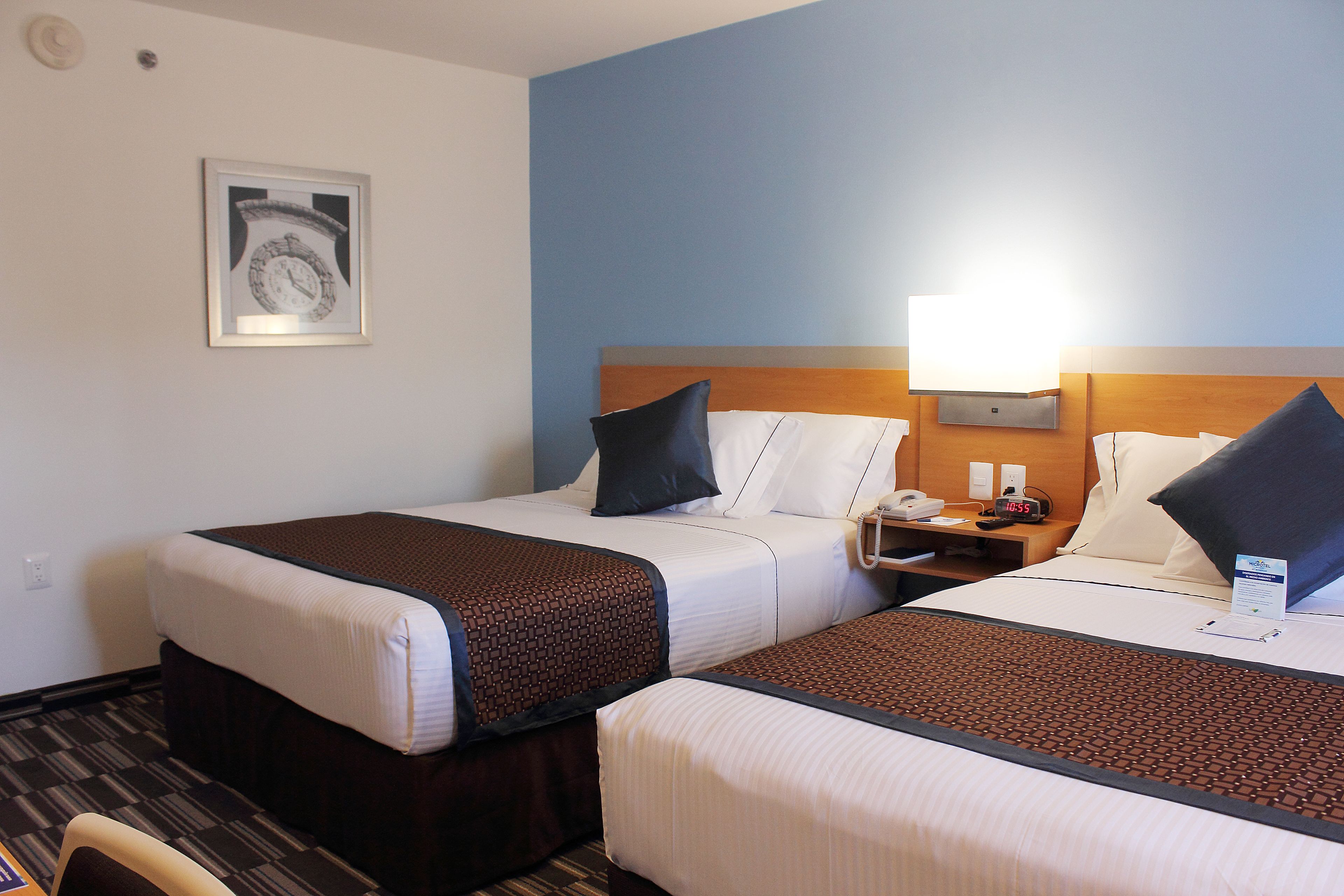 A hotel room with two beds, a nightstand with a lamp, and a framed picture on the wall.