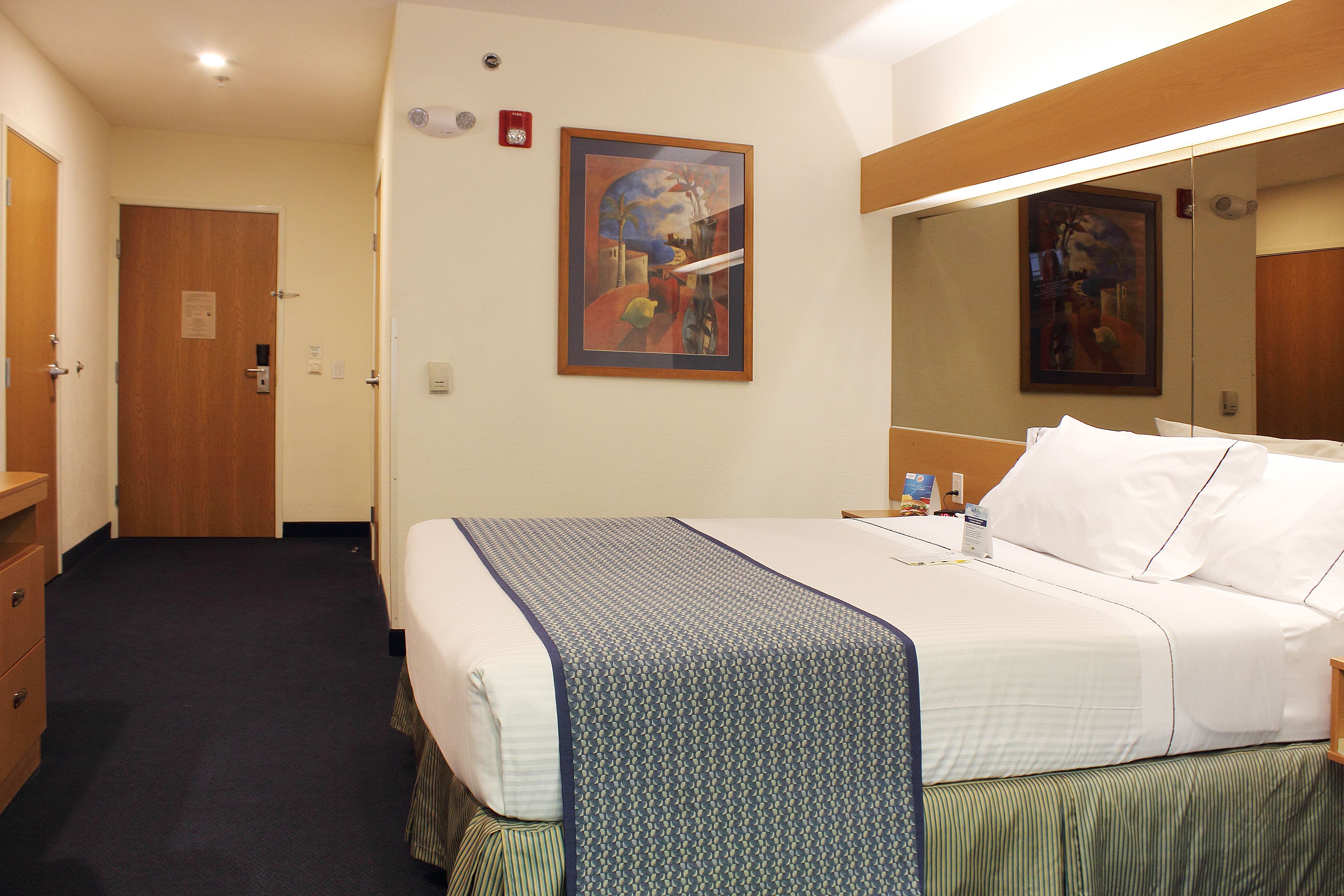 A hotel room with a bed, a dresser, a painting on the wall, and a mirror.