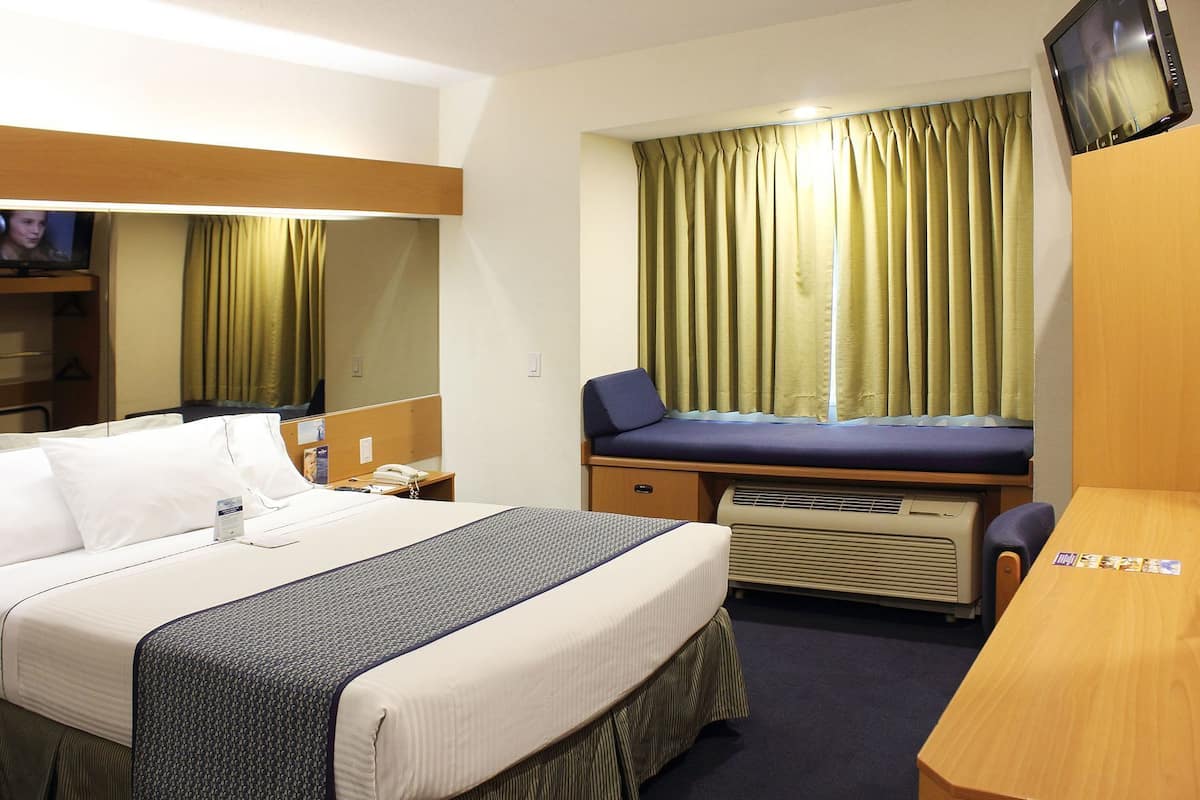 A hotel room with a bed, a desk, a chair, a television, a window with curtains, and a mirror.