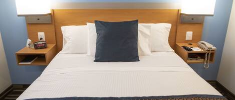 Habitación de hotel con una cama, dos mesitas de noche, una lámpara, un reloj y un teléfono.
