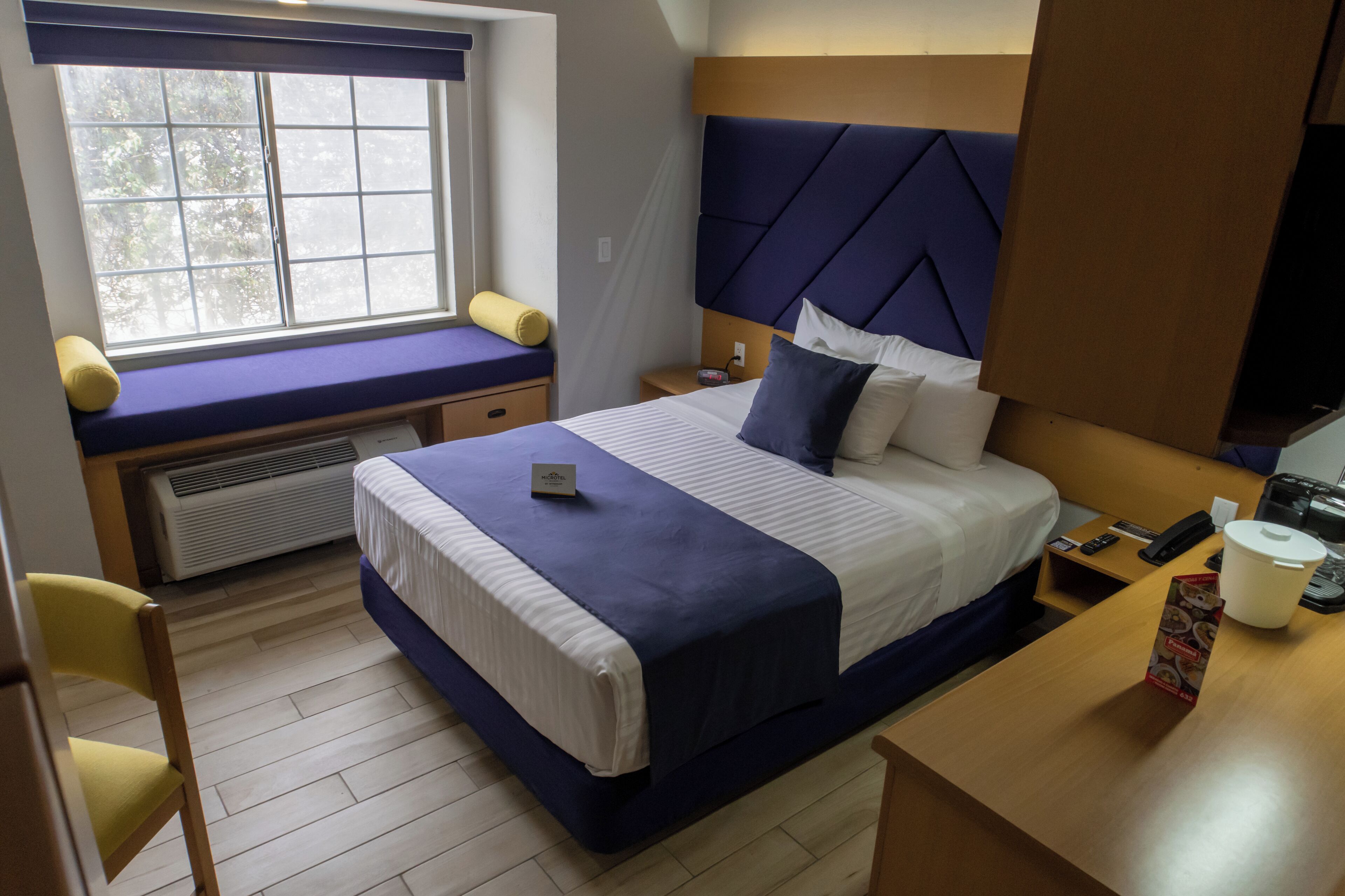 A hotel room with a bed, a window seat, a desk, and a chair.