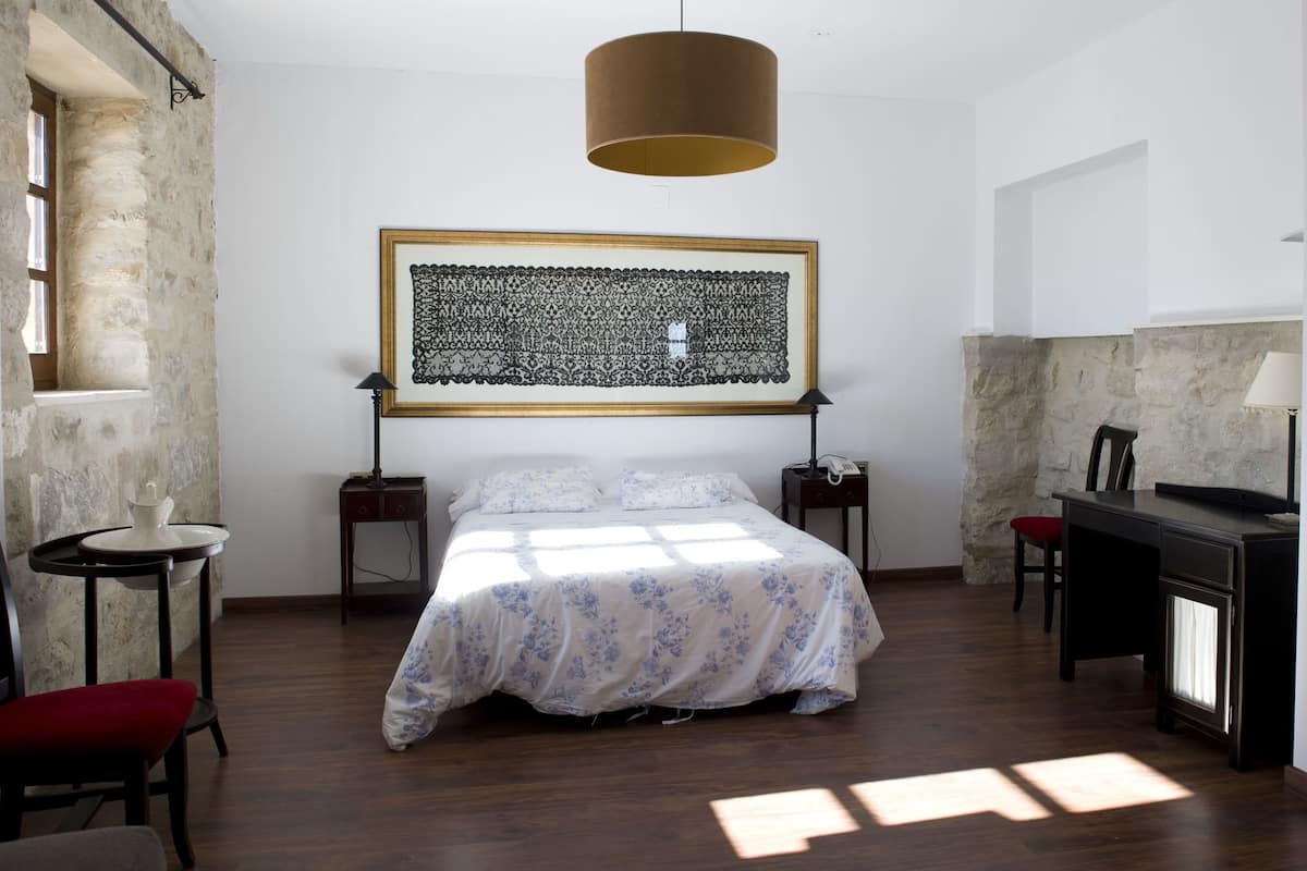A bedroom with a bed, a desk, a chair, a lamp, and a fireplace.