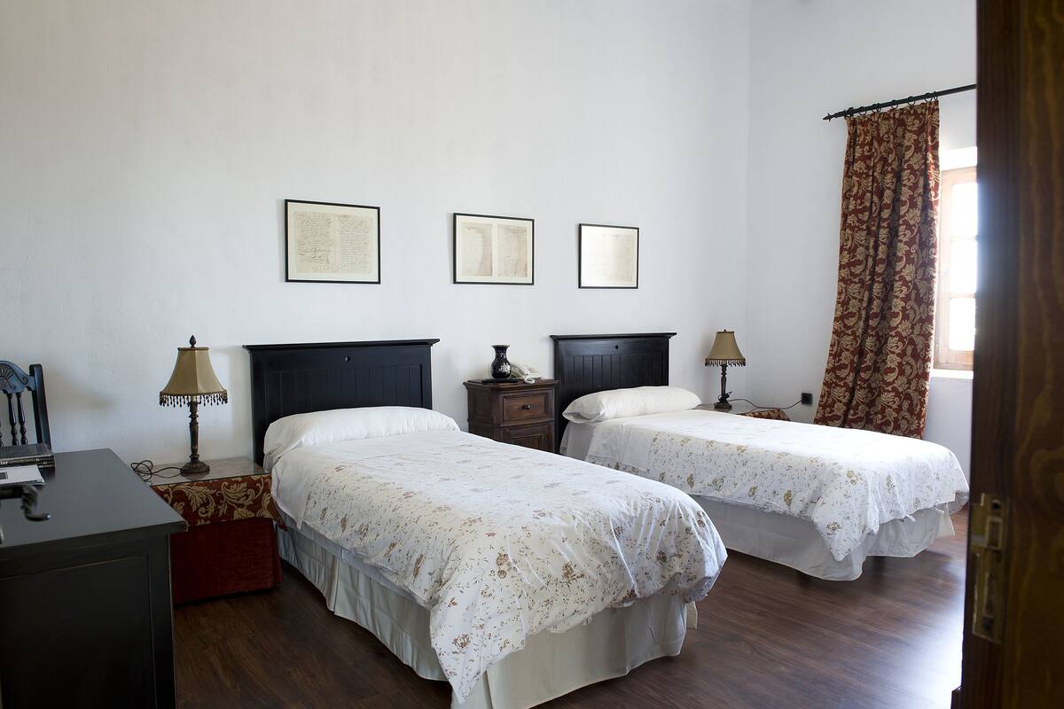 A room with two beds, a desk, a chair, and a window with curtains.
