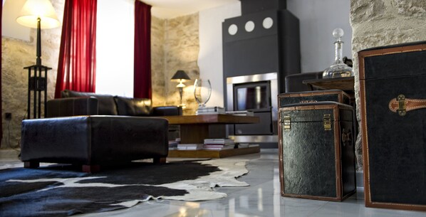 A living room with a fireplace, leather sofa, and vintage trunks. - Rusticae Las Casas del Cónsul (Úbeda)