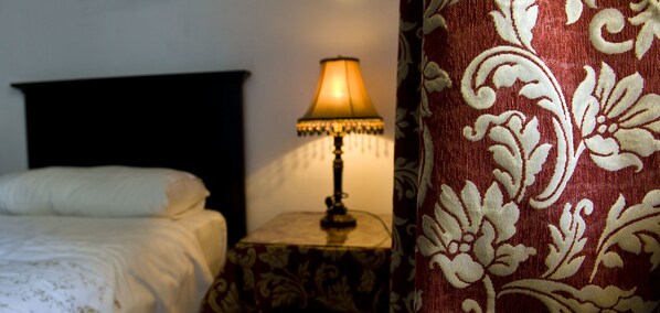 A bed with a white comforter and a dark headboard, a bedside table with a lamp, and a red patterned curtain. - Rusticae Las Casas del Cónsul (Úbeda)