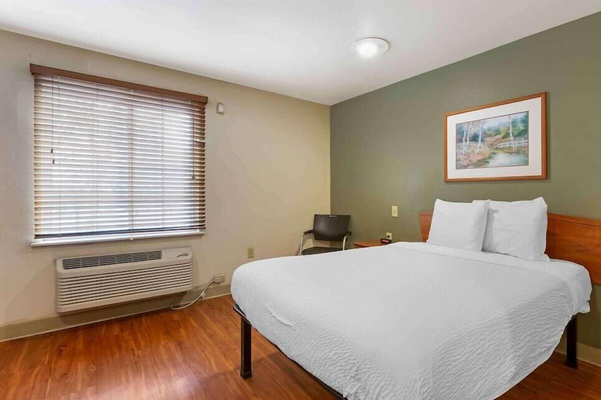 Een slaapkamer met een bed, een stoel, een verwarming en een foto aan de muur.