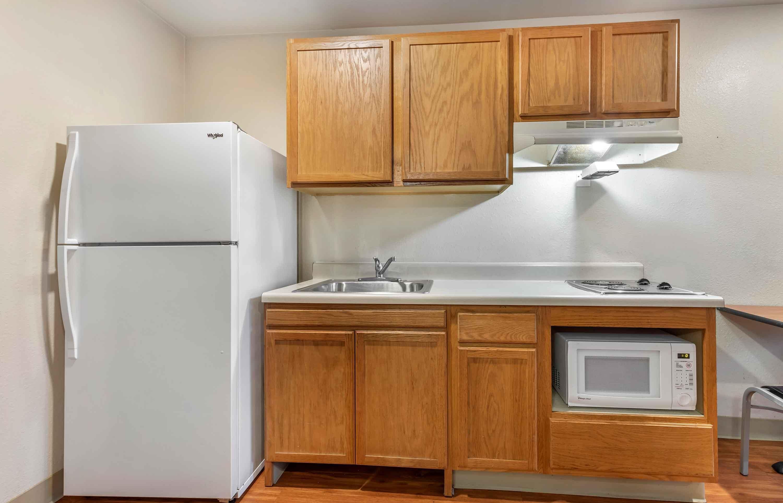 A compact kitchen with wooden cabinets, a white refrigerator, a microwave, and a sink.