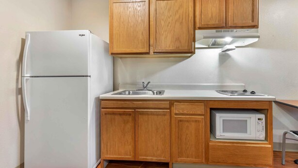 Una cocina compacta con gabinetes de madera, un refrigerador blanco, un microondas y un lavamanos.