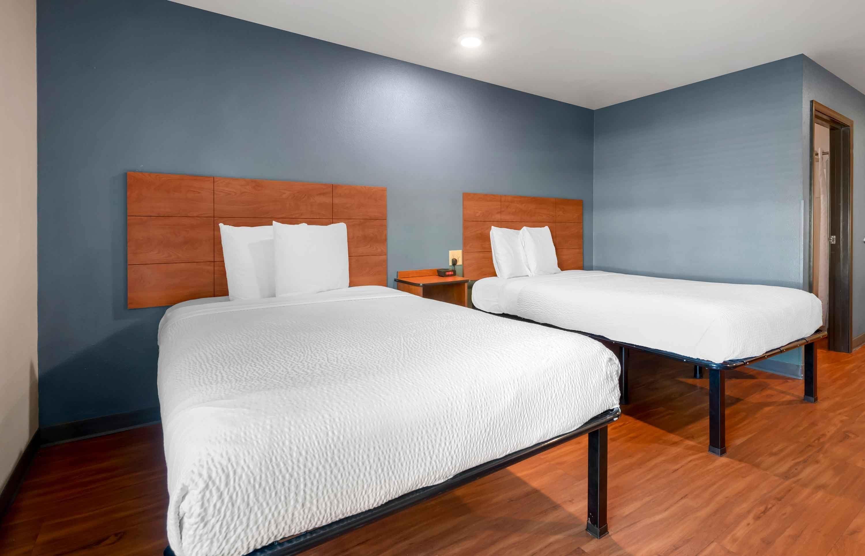 Habitación de hotel con dos camas y cabeceros de madera, y una pared azul.