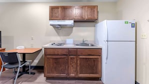 A compact kitchen with wooden cabinets, a white refrigerator, and a sink. - Extended Stay America Select Suites - Lubbock - West (Lubbock)
