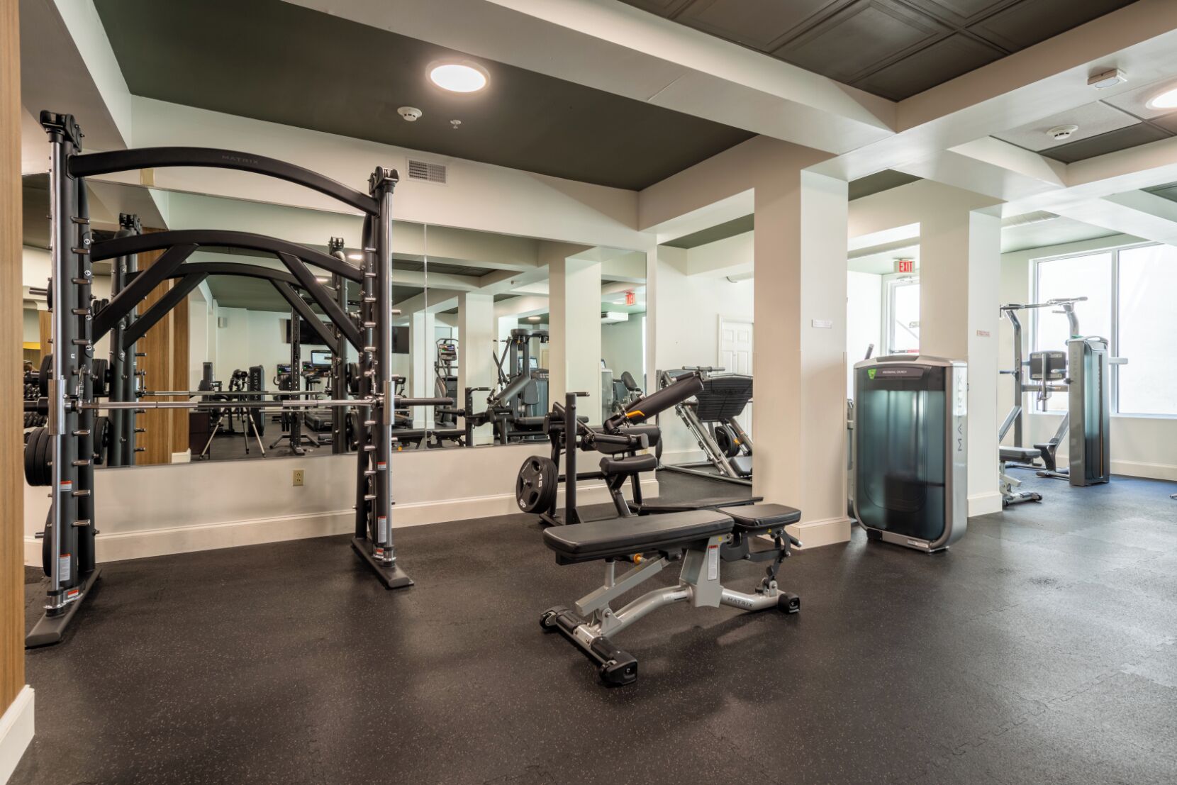 A gym with weightlifting equipment, mirrors, and a cardio machine.
