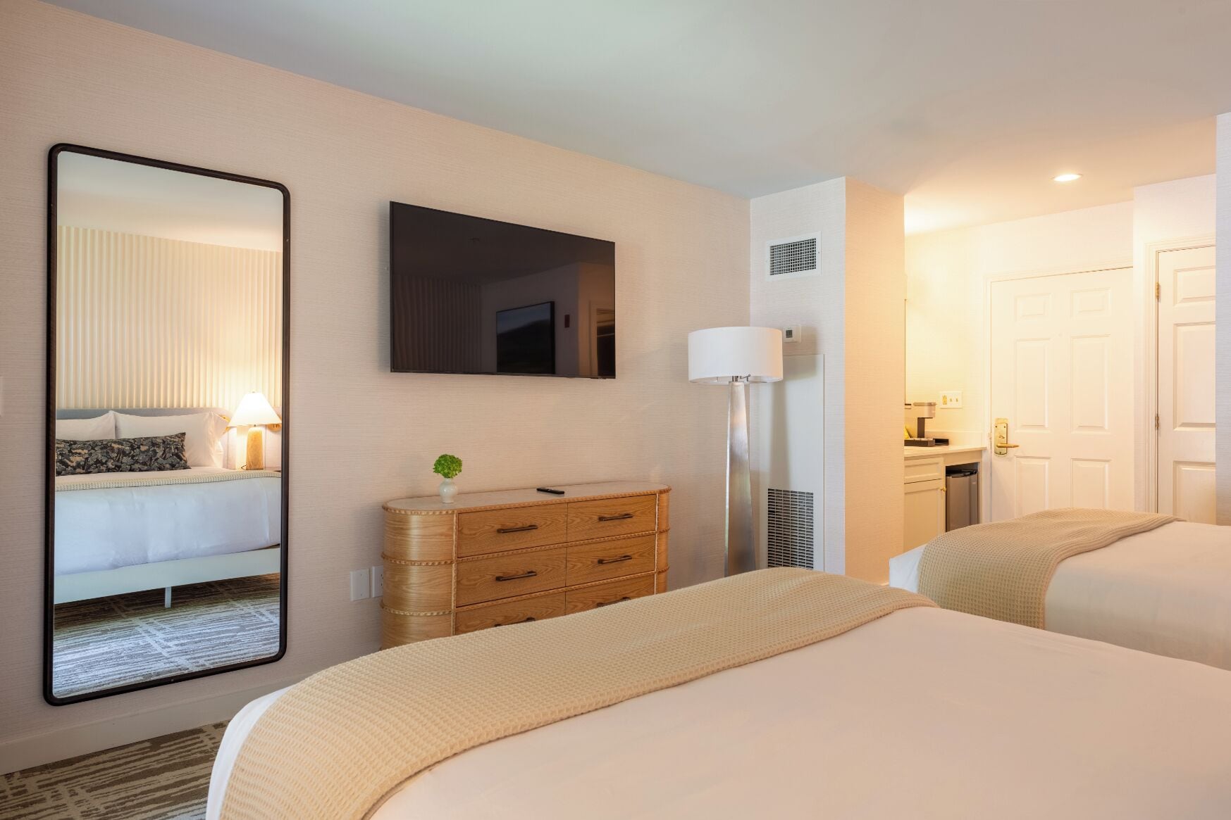 A hotel room with a bed, a dresser, a mirror, a flat-screen TV, a lamp, and a door.