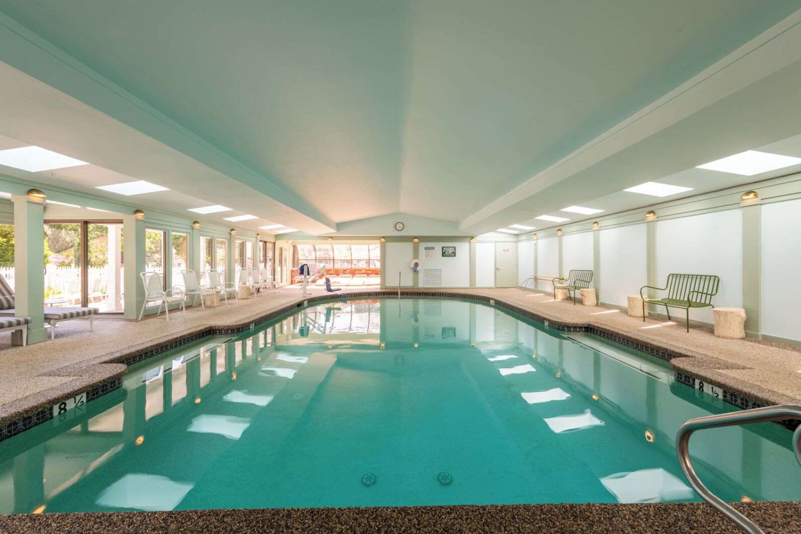 Una piscina interior con agua cristalina, borde de azulejos y techo iluminado por el sol.