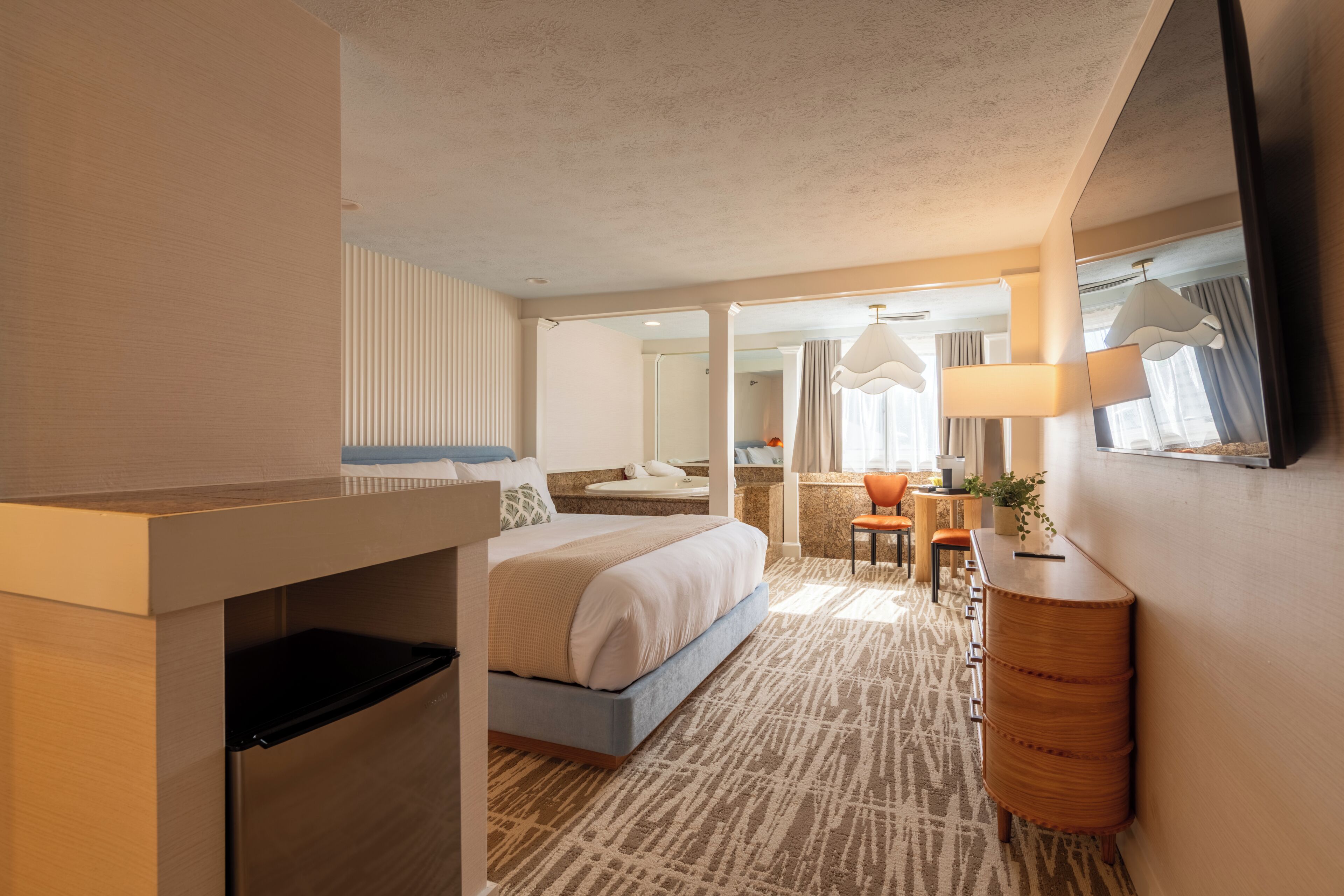 Habitación de hotel con cama, escritorio, silla, espejo y ventana.