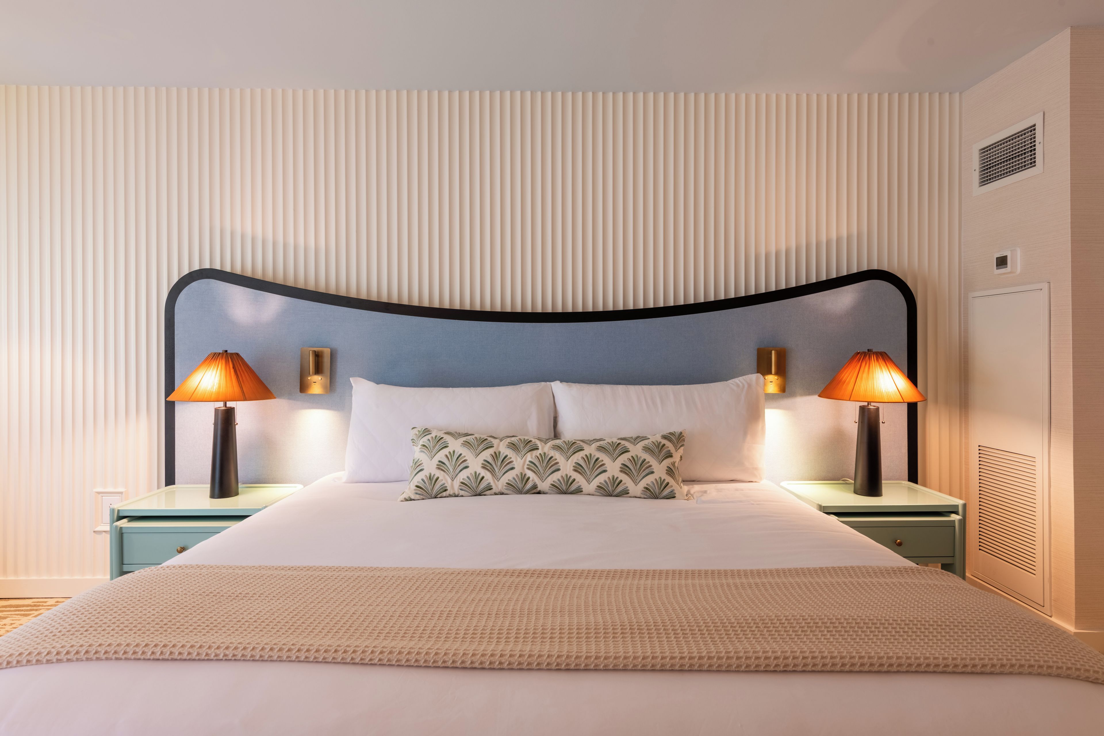 A neatly made bed with a patterned pillow, two bedside lamps, and a textured throw blanket.