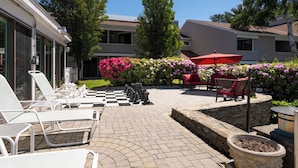 A courtyard with lounge chairs, a chessboard, and a red umbrella. - The Meadowmere Resort (Ogunquit)