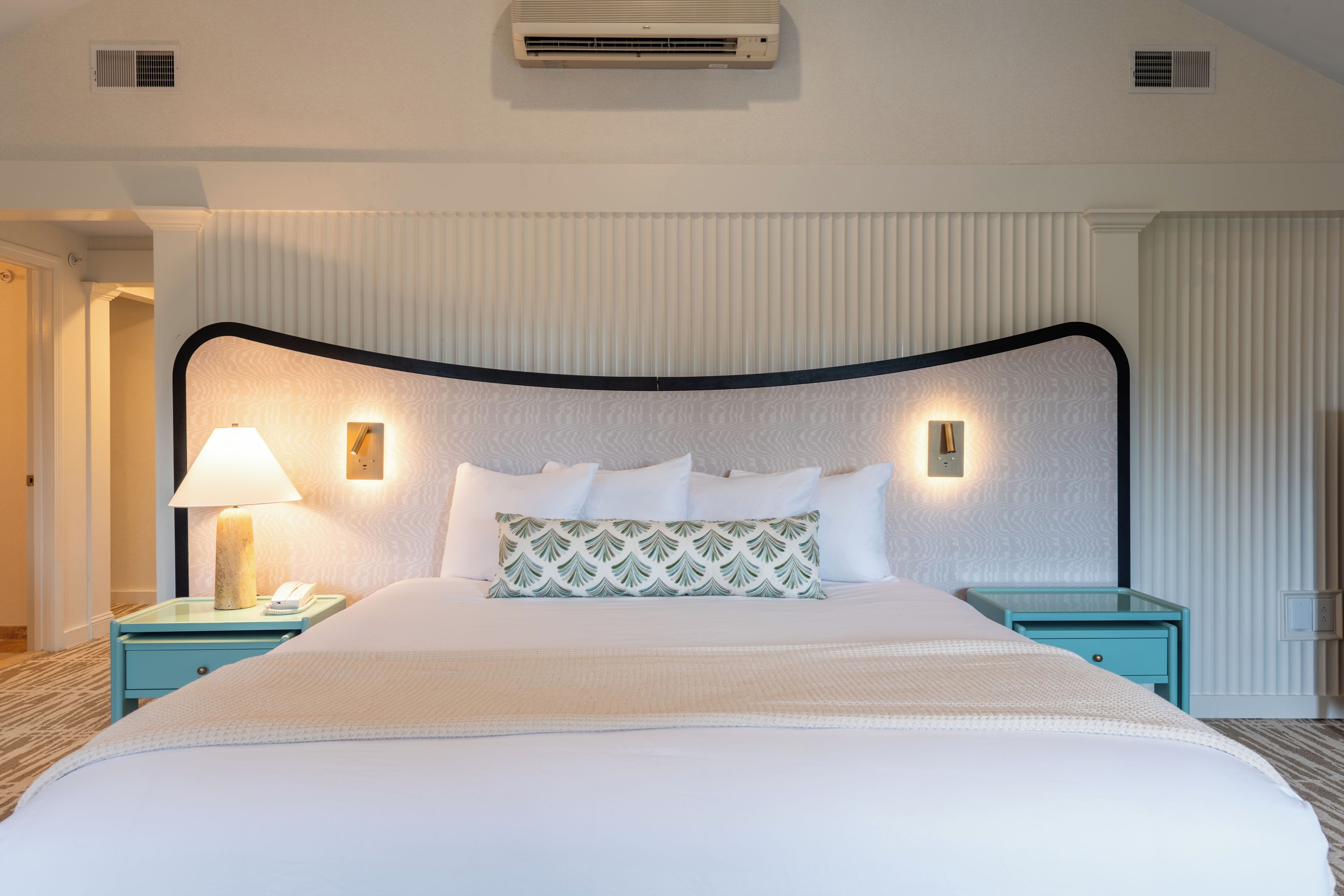 Une chambre d’hôtel avec un grand lit, deux tables de chevet, une lampe et un appareil de climatisation.