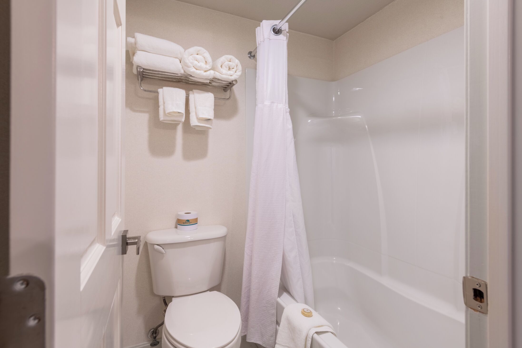 Ein Badezimmer mit Toilette, einer Dusche mit weißem Vorhang und einem Handtuchhalter mit ordentlich gefalteten Handtüchern.