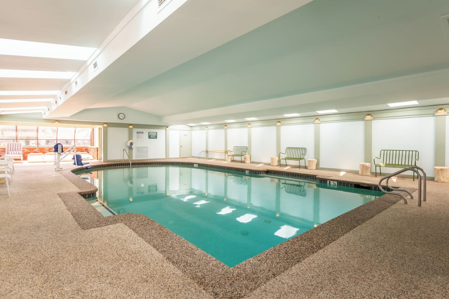 An indoor swimming pool with clear water, surrounded by benches and a tiled floor.