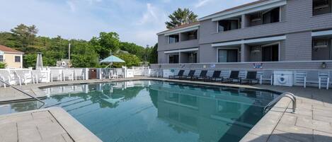 A swimming pool with lounge chairs and a covered area, surrounded by a building with multiple balconies.
