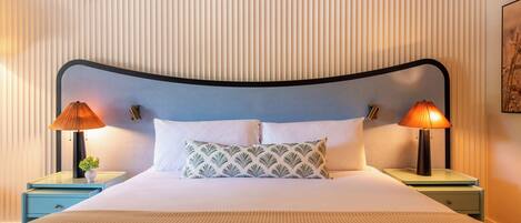 A neatly made bed with a patterned pillow, two bedside lamps, and a wall with vertical lines.