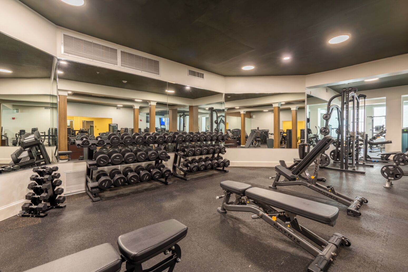 A gym with weightlifting equipment, benches, and a mirrored wall.