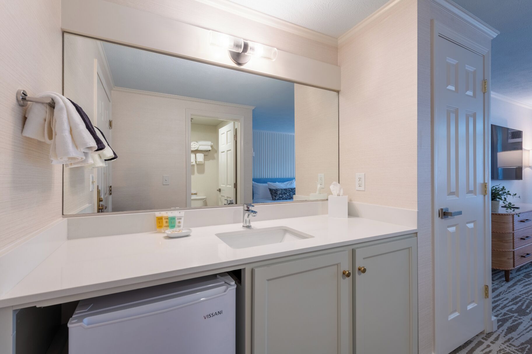 A bathroom with a large mirror, a sink, a towel rack, and a VISSANI dishwasher.