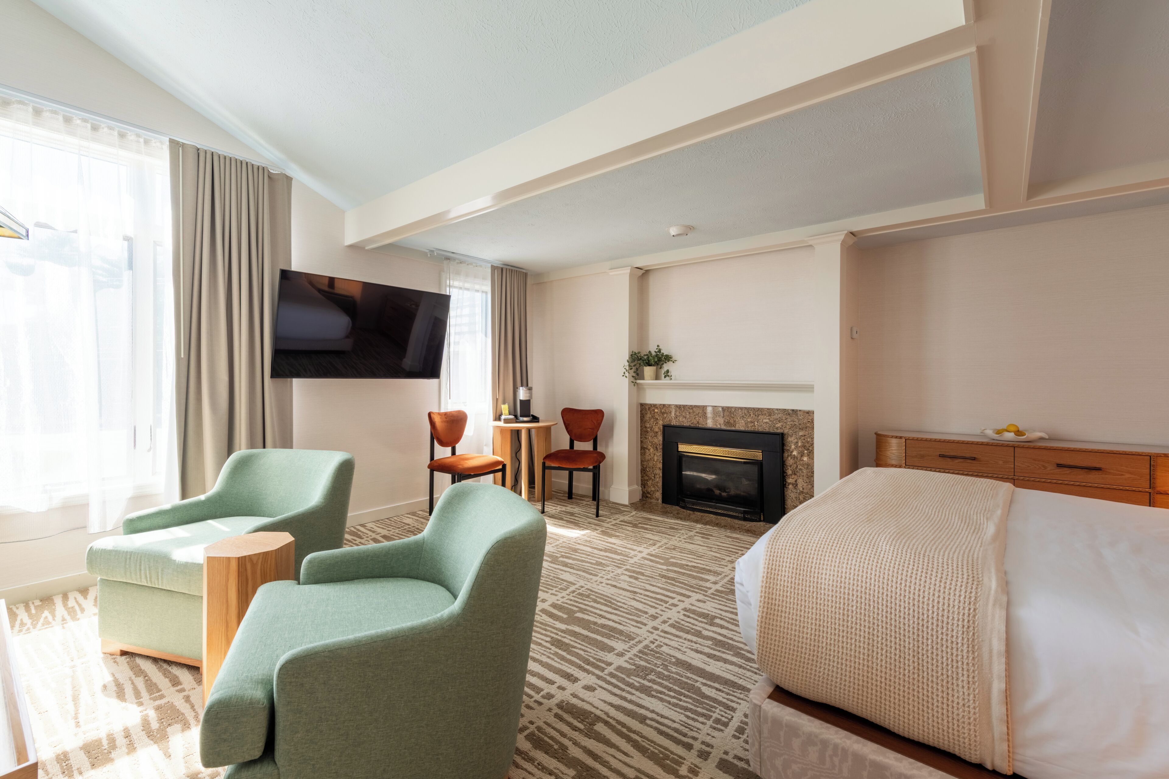 A hotel room with a bed, two armchairs, a TV, a fireplace, and a view of the outdoors.