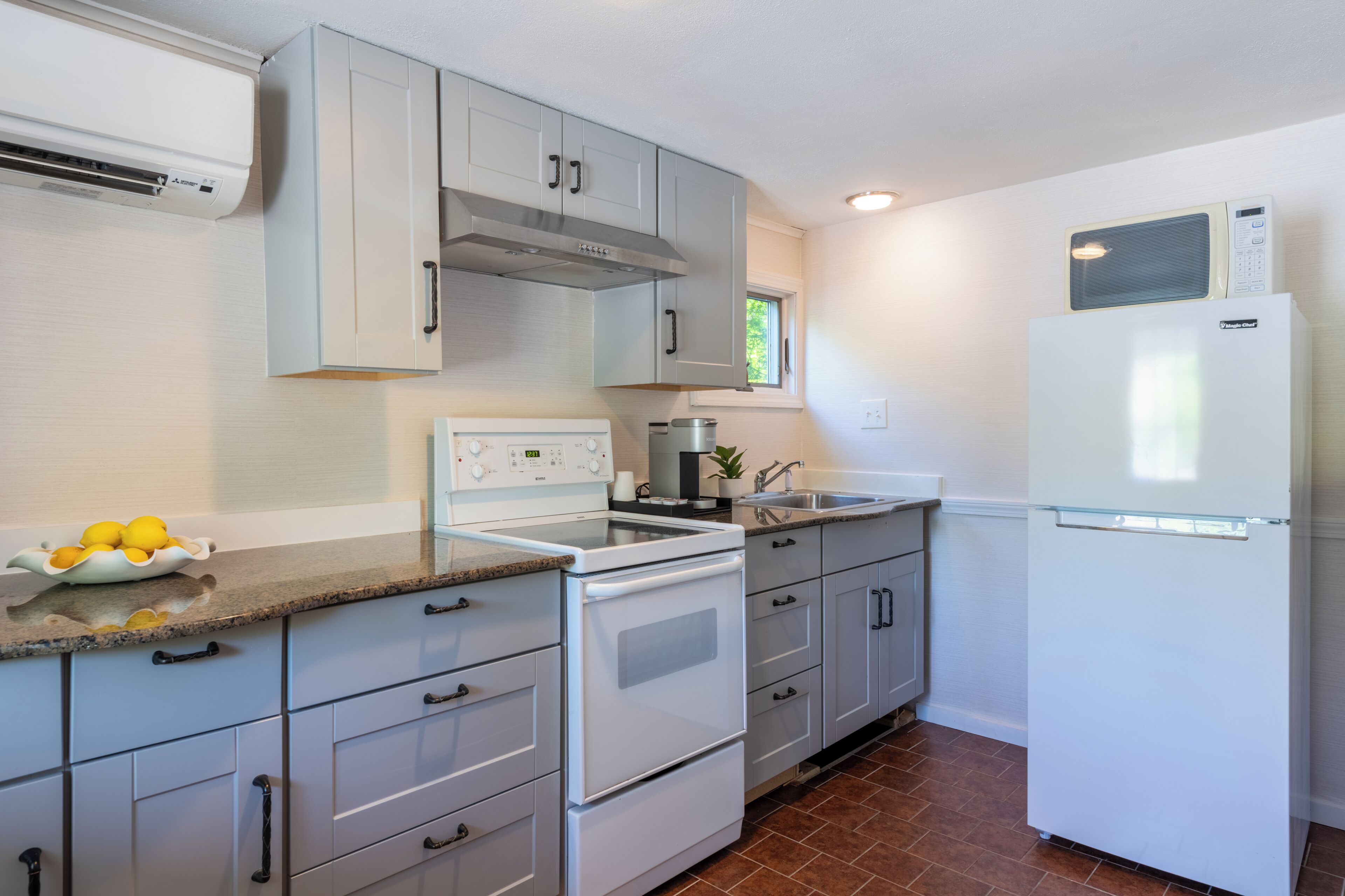 A kitchen with white cabinets, a stove, a refrigerator, and a bowl of lemons on the counter.