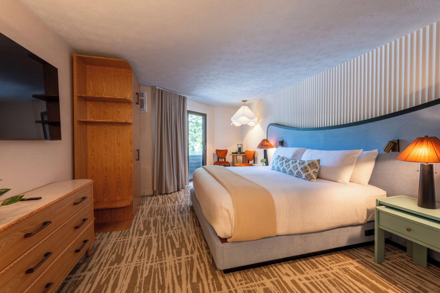 Una habitación de hotel con cama, cómoda, mesita de noche, lámpara y ventana con cortinas.