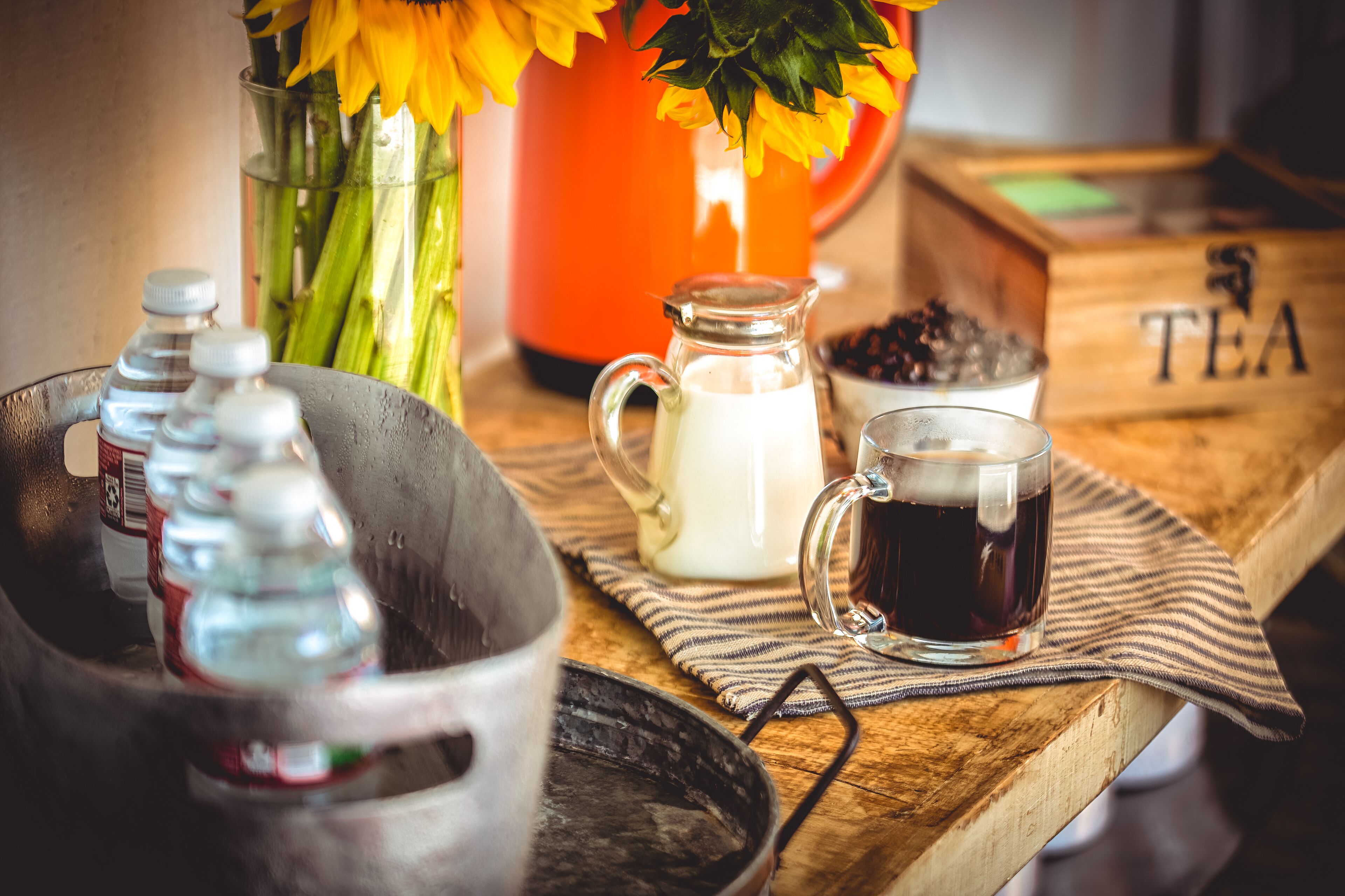 A wooden table with a glass pitcher, a glass cup, and a bottle of milk.