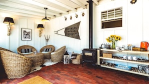 A cozy living room with wicker furniture, a wood-burning stove, and a wall-mounted sign. - Stables Inn (Paso Robles)