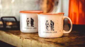 Two white mugs with orange rims and a cowboy and horse illustration, labeled "Stables Inn."