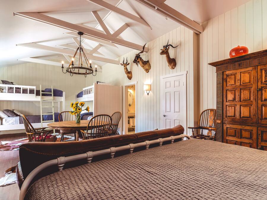A room with a bunk bed, a dining table with chairs, a chandelier, and wooden cabinets.