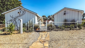 A building with a mural of a moose, a stone pathway, and a fenced area with small plants. - Stables Inn (Paso Robles)