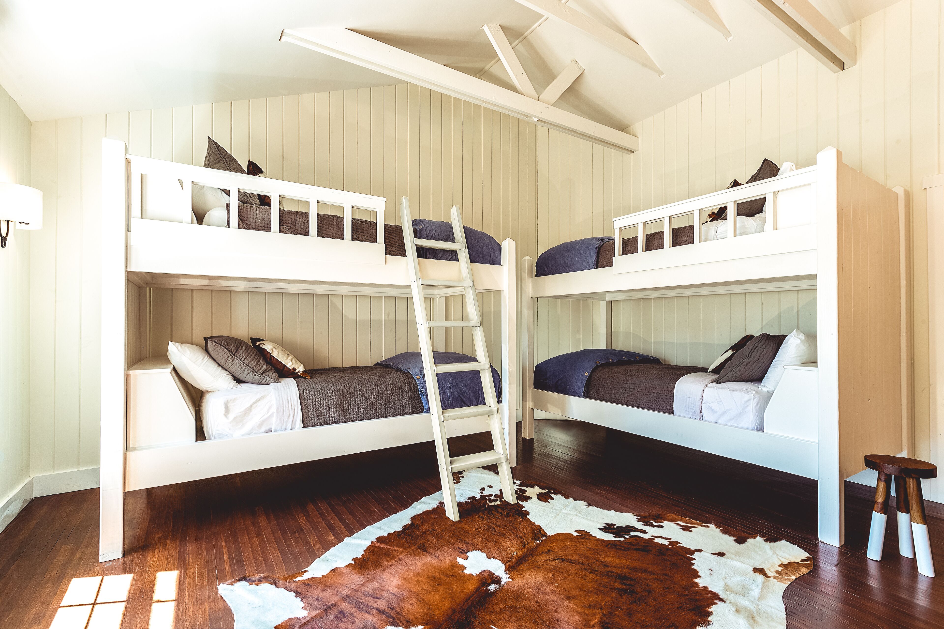 Quarto com beliche, escada, piso de madeira e tapete de couro.