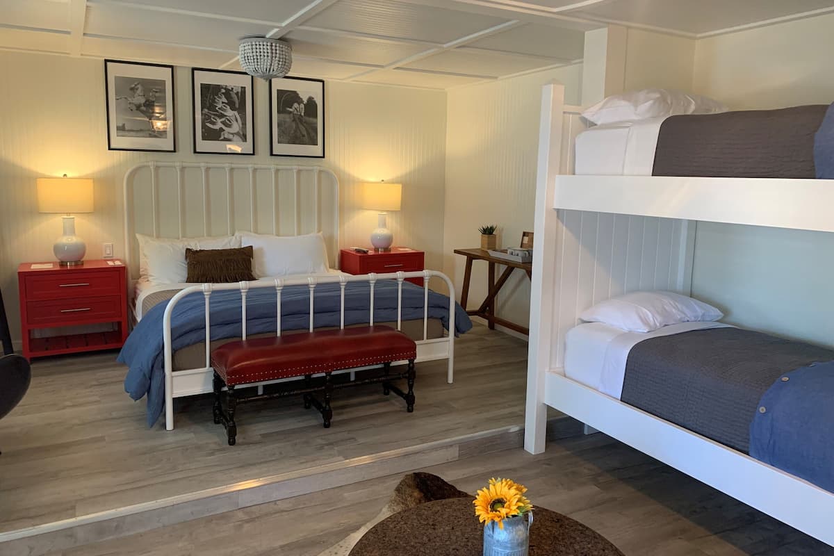 Ein Schlafzimmer mit einem Etagenbett, einem Einzelbett, einem Nachttisch, einer Lampe und gerahmten Bildern an der Wand.