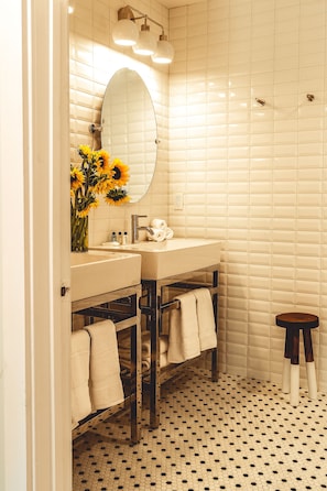 A bathroom with a white tiled wall, a round mirror, a sink, and a toilet. There are towels hanging on a rack and a small stool.
