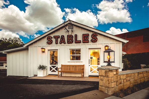 A white building with a sign reading "STABLES" and a wooden bench in front.
