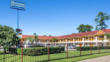 A motel with a signboard, fenced parking, and a building with a red roof.