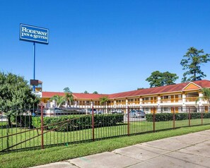 A motel with a signboard, fenced parking, and a building with a red roof.