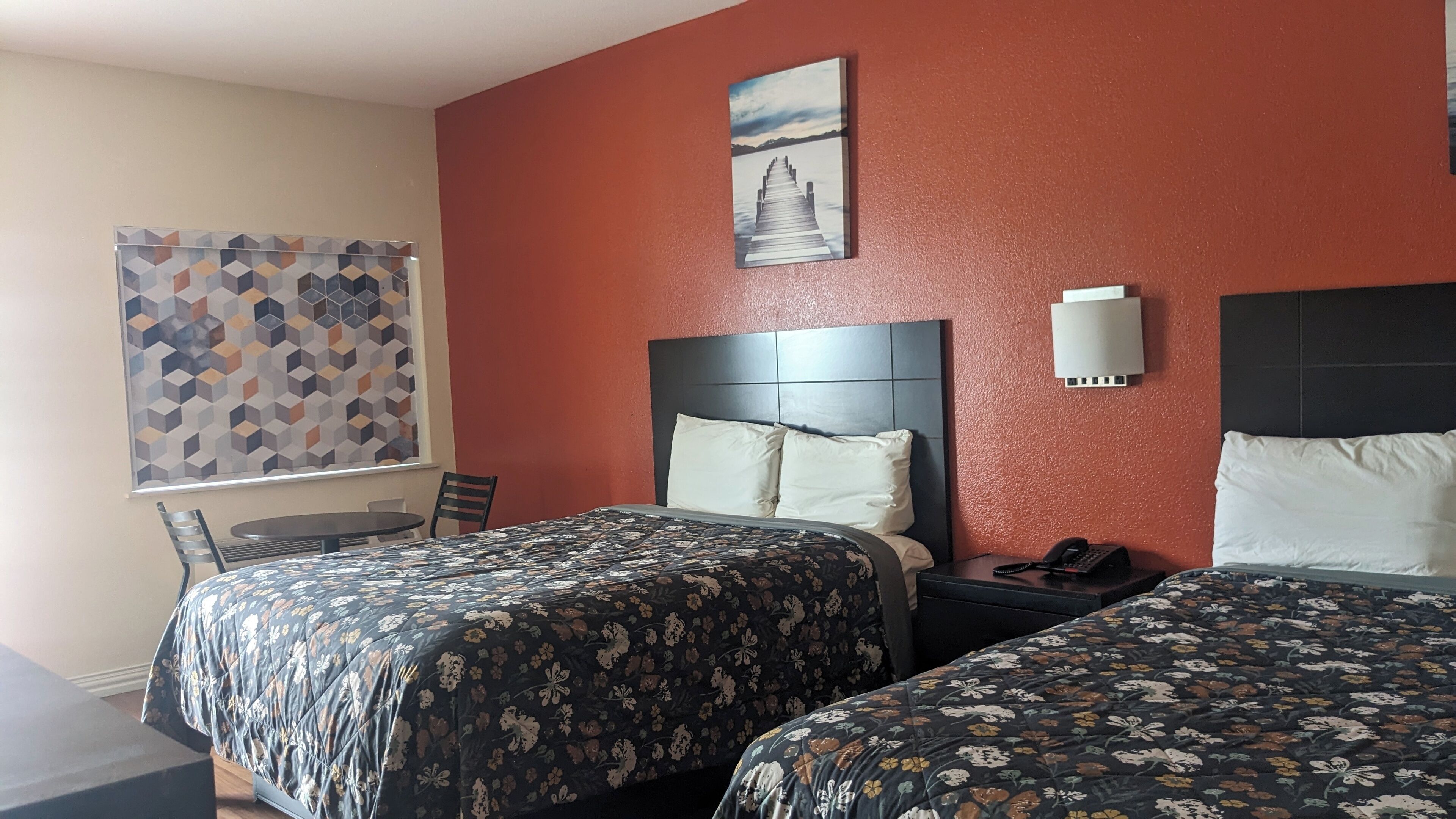 Une chambre d’hôtel avec deux lits, un bureau, une chaise, un téléphone et un tableau au mur.