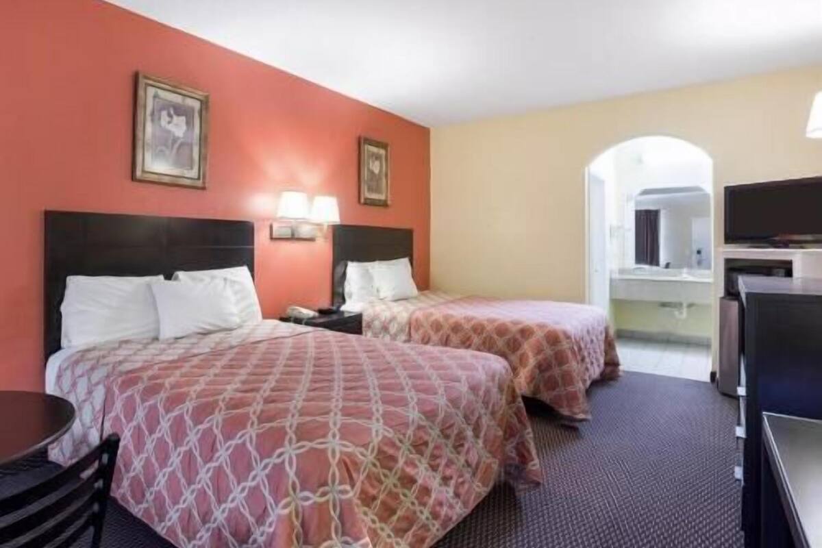 A hotel room with two beds, a TV, and a desk.