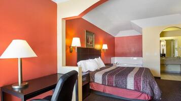 A hotel room with a bed, desk, chair, and a bathroom with a bathtub.